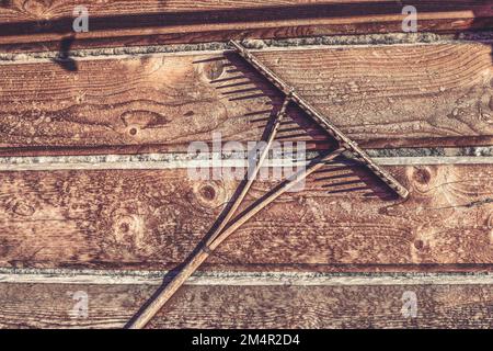 Holzrechen hängt an der Wand eines Holzhauses. Altes Bauernwerkzeug. Hochwertiges Foto Stockfoto