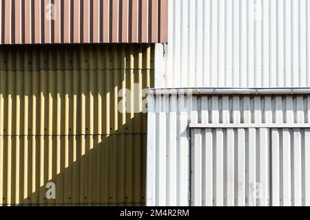 Die Metallfassaden eines Industriegebäudes in Weiß, Braun und Grün sind gestaffelt und erscheinen abstrakt. Stockfoto