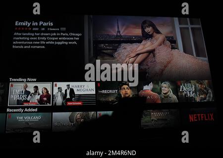 Netflix App auf dem fernsehbildschirm, die die Fernsehserie Emily in Paris hervorhebt, mit dem Schatten einer Fernbedienung vor dem Fernsehbildschirm Stockfoto