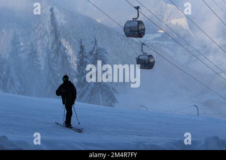 Skifahrer in schwarz gekleidet vor Gondeln auf einer Schneehügel im Winter in den Schweizer Alpen in Verbier, Wallis, Schweiz. Coole Atmosphäre und Atmosphäre Stockfoto