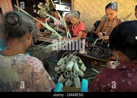 Frauen, die Souvenirtaschen für Besucher herstellen, vor der Prozession vor der Hochzeit mit einem traditionellen königlichen Führer und einer australischen Frau, fotografiert im Dorf Prailiu, East Sumba, Sumba Island, Indonesien. Stockfoto