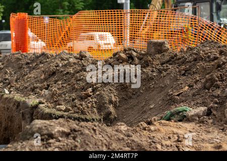 Aushub auf der Baustelle. Rohrleitungen in der Stadt verlegen. Ausgehobene Erde. Kabelgraben. Bauarbeiten. Stockfoto