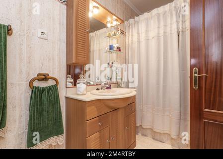 Toilette mit Holzwaschtisch mit Türen und Schubladen und Spiegel mit Glasregalen und passenden Wandleuchten Stockfoto