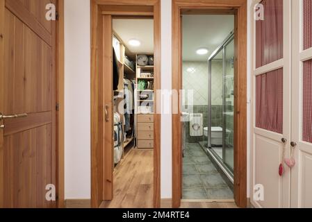 Schlafzimmer mit weißem Kleiderschrank und Schrank mit Schubladen und Regalen und Bad mit bodenebener Dusche und grünen Fliesen Stockfoto