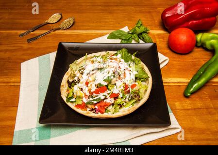 Eine Art Salatpizza mit viel Soße und Salat mit Tomaten Stockfoto