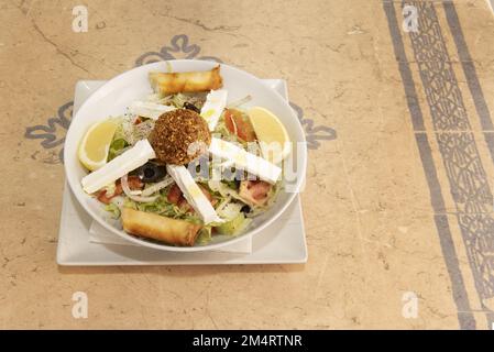 Ein marokkanischer Salat mit frischem Fetakäse, Pfeffer, schwarzen Oliven, Falafel-Kugel, weißen Zwiebeln und Eisbergsalat mit Zitronenschnitten Stockfoto
