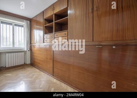 Zimmer mit Möbeln an der Wand und Klappbetten aus hellem Holz sowie doppelverglasten Aluminiumfenstern mit Gitterstäben Stockfoto