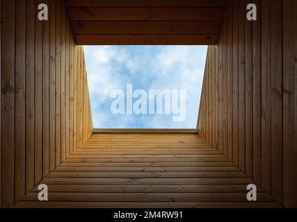 Dachverlängerung, Dachfenster. Studentenfenster in einer hölzernen Decke mit Blick auf den blauen Himmel. Sonnenlicht dringt durch ein Dachfenster in das Zimmer ein Stockfoto