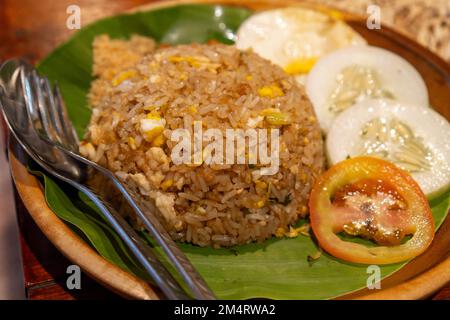 Gebratener Reis, gemischt mit Ei, Gurke und ​​tomatoes-Scheiben. Serviert auf einem Holzteller mit Bananenblättern Stockfoto