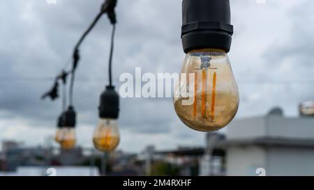 Die Lichter hängen am Nachmittag auf. Das Licht ist an. Im Café vor dem Hintergrund des Abendhimmels sind mehrere Lichter zu sehen Stockfoto