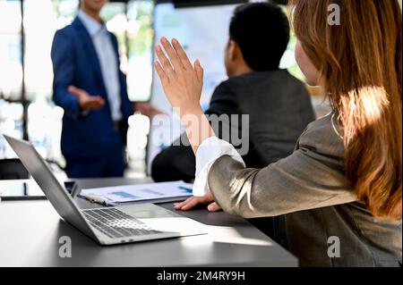 Eine wunderschöne und professionelle asiatische Geschäftsfrau, die während des Meetings mit einem Finanzanalytiker Hand hebt und ein paar Fragen stellt. Rückansicht Stockfoto
