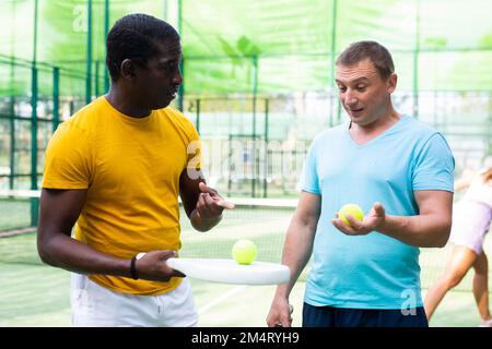 Zwei Männer mit Schlägern in den Händen plaudern nach dem Padel-Spiel auf dem Tennisplatz Stockfoto