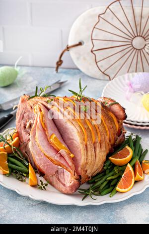 Osterschinken gefüllt mit Orangenscheiben und Kräutern, glasierter Schinken in Spiralscheiben Stockfoto