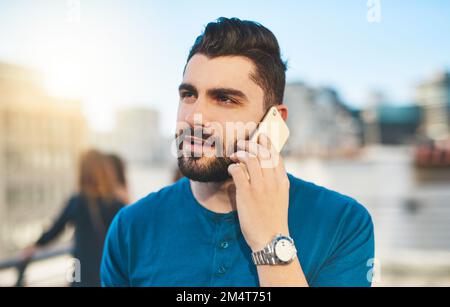 Klar, lass hören. Ein gutaussehender junger Mann, der telefoniert, während er draußen steht. Stockfoto