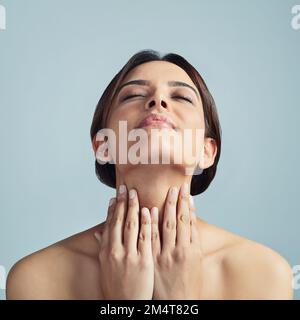 Hautpflege war noch nie so einfach. Eine junge Frau, die ihre Haut vor grauem Hintergrund berührt. Stockfoto