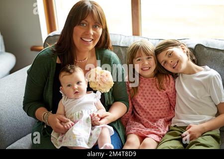 Eine große, gesegnete Familie. Porträt einer Mutter, die sich mit ihren drei kleinen Kindern zu Hause anfreundet. Stockfoto