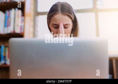 Ich hoffe, ich beende diesen Auftrag pünktlich. Eine junge Frau, die gestresst aussieht, während sie hinter einem Laptop sitzt. Stockfoto