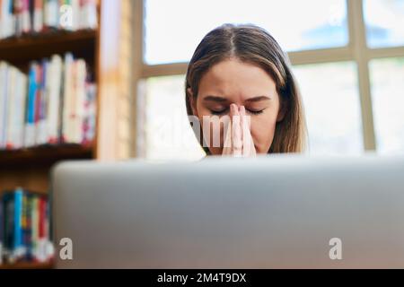 Ich hoffe, ich beende diesen Auftrag pünktlich. Eine junge Frau, die gestresst aussieht, während sie hinter einem Laptop sitzt. Stockfoto