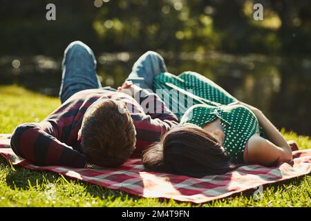 Diese faulen Nachmittage mit dem, den du liebst. Ein junges Paar, das auf einer Picknickdecke im Park liegt. Stockfoto