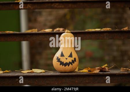 Bemalter Kürbis steht auf eisernen Stufen in trockenen Herbstblättern Vorbereitung auf halloween, halloween Stockfoto