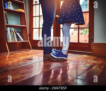 Die Hölle sei da, um sie durchs Leben zu führen. Ein kleines Mädchen, das zu Hause auf den Füßen ihres Vaters steht. Stockfoto