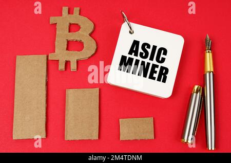 Business- und Bitcoin-Konzept. Auf einer roten Oberfläche liegen ein Bitcoin-Symbol, ein Diagramm, ein Stift und ein Notizblock mit der Aufschrift ASIC Miner Stockfoto