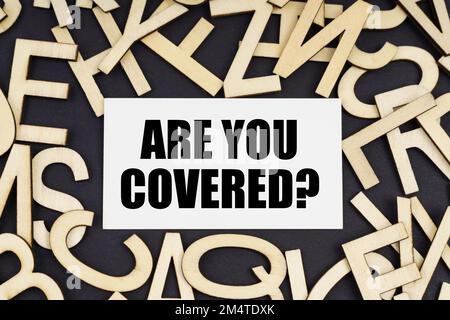 Finanz- und Wirtschaftskonzept. Auf einer schwarzen Oberfläche befinden sich Holzbriefe und eine Visitenkarte mit der Aufschrift – SIND SIE VERDECKT Stockfoto