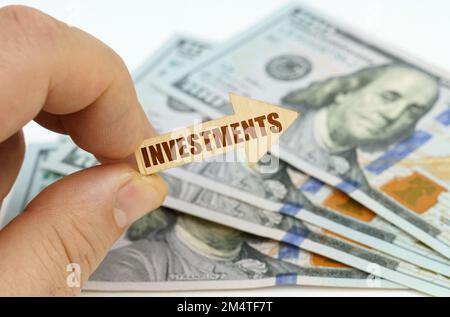 Geschäfts- und Finanzkonzept. In den Händen eines Mannes ist ein Pfeil mit der Inschrift - Investitionen, im Hintergrund sind Dollar. Stockfoto