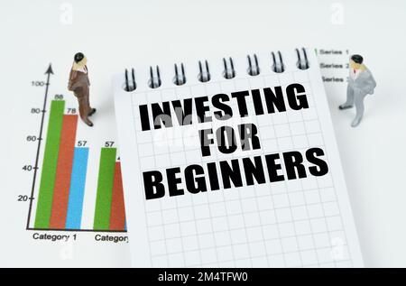 Geschäfts- und Finanzkonzept. Auf der Karte sind Miniaturfiguren von Geschäftsleuten und ein Notizblock mit der Inschrift "INVESTITION FÜR ANFÄNGER" Stockfoto