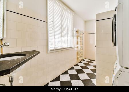 Ein Bad mit schwarz-weiß karierten Fliesen auf dem Boden, zusammen mit einer Toilette in der Ecke neben dem Fenster Stockfoto