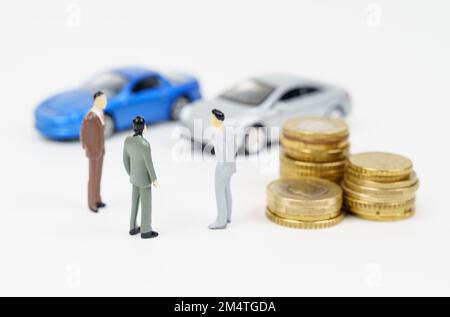 Autogeschäft. Drei Miniaturfiguren eines Geschäftsmanns, Münzen und Autos im Hintergrund. Stockfoto