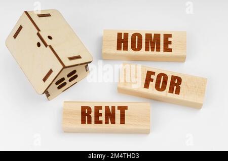 Geschäfts- und Immobilienkonzept. Auf einer weißen Oberfläche, einem hölzernen Spielzeughaus und Bausteinen mit der Aufschrift "Home for Rent" Stockfoto