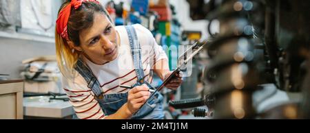 Eine Mechanikerin, die die Motorraddokumentation in der Garage ausfüllt Stockfoto