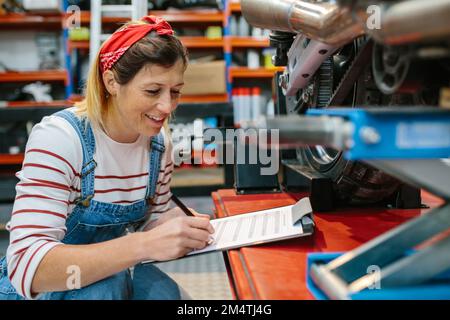 Eine Mechanikerin, die die Motorraddokumentation in der Garage ausfüllt Stockfoto