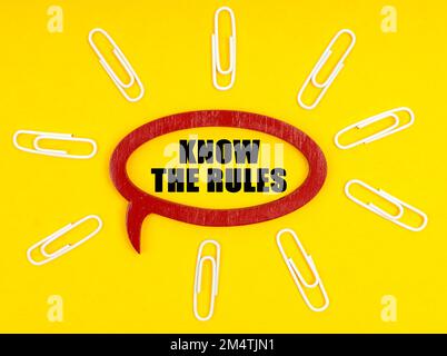 Business- und Economy-Konzept. Auf der gelben Oberfläche befinden sich Büroklammern und eine Platte, auf der die Inschrift die REGELN KENNT Stockfoto