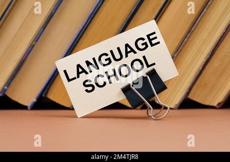 Bildungs- und Wissenschaftskonzept. Auf dem Tisch vor dem Hintergrund von Büchern liegt eine Visitenkarte mit der Inschrift - Sprachschule Stockfoto