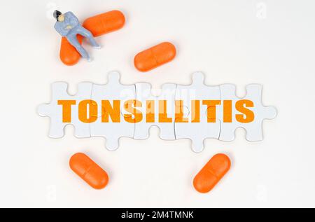 Medizinisches Konzept. Auf der weißen Oberfläche der Tablette, eine Miniaturfigur des Menschen und Rätsel mit der Inschrift - Tonsillitis Stockfoto
