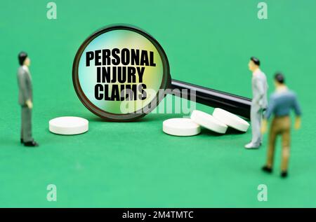 Medizinisches Konzept. Auf einer grünen Oberfläche sind Pillen, Miniaturfiguren von Menschen und eine Lupe mit der Inschrift "Persönliche Verletzungsansprüche" Stockfoto
