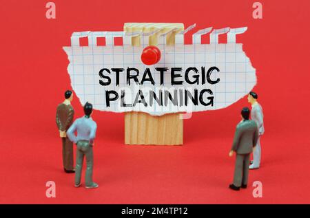 Geschäftskonzept. Auf rotem Hintergrund sind Miniaturfiguren von Leuten, die eine Anzeige mit der Inschrift "STRATEGISCHE PLANUNG" ansehen Stockfoto