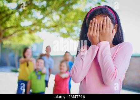 Ich wünschte, das Mobbing könnte aufhören. Ein junges Mädchen, das ihr Gesicht verdeckt, während sie draußen gemobbt wird. Stockfoto