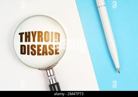 Medizinisches Konzept. Auf einer weißen - blauen Oberfläche sind ein Stift und eine Lupe mit der Inschrift - SCHILDDRÜSENERKRANKUNG Stockfoto