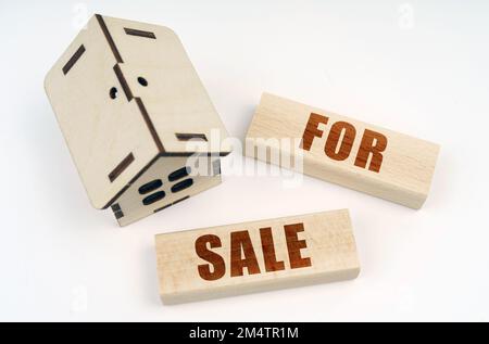 Geschäfts- und Immobilienkonzept. Auf einer weißen Oberfläche, einem hölzernen Spielzeughaus und Bausteinen mit der Aufschrift „zum Verkauf“ Stockfoto