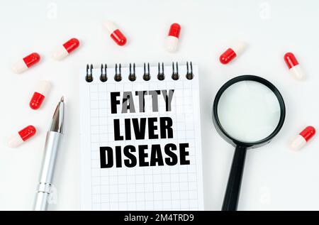Medizinisches Konzept. Auf einer weißen Oberfläche befinden sich Tabletten, ein Stift, eine Lupe und ein Notizblock mit der Aufschrift - FETTLEBERERKRANKUNG Stockfoto