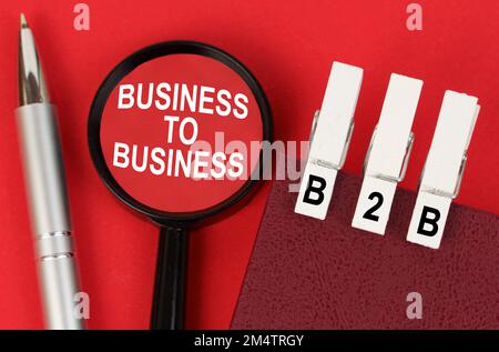 Geschäftskonzept. Auf der roten Oberfläche liegen ein Stift, ein Notizbuch mit Wäscheklammern - B2B und eine Lupe mit der Aufschrift - Business to Business Stockfoto