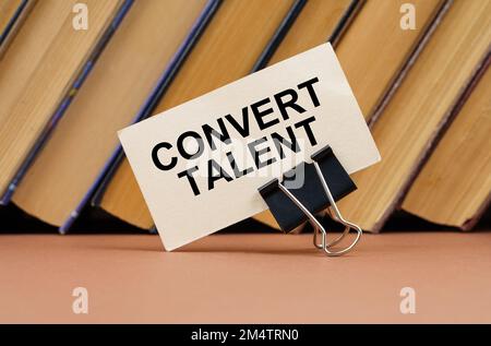 Bildungs- und Wissenschaftskonzept. Auf dem Tisch vor dem Hintergrund von Büchern befindet sich eine Visitenkarte mit der Aufschrift „Convert Talent“ Stockfoto