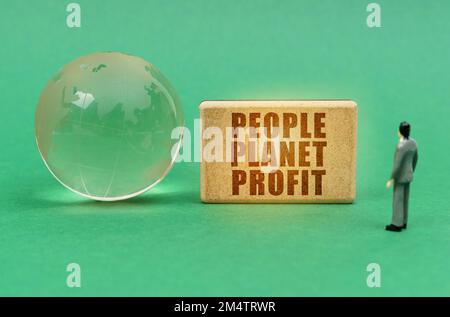 Ökologisches Konzept. Auf der grünen Oberfläche sehen Sie eine Kugel und eine Figur eines Mannes, der auf ein Schild mit der Inschrift "People Planet Profit" schaut Stockfoto