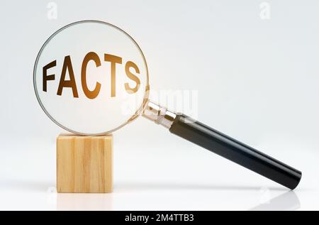 Wirtschaftskonzept. Auf einer weißen Oberfläche befinden sich ein Würfel und eine Lupe, in der sich die Inschrift befindet - FAKTEN Stockfoto