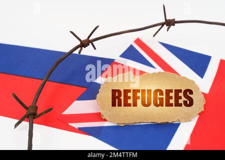 Politisches Konzept. Auf den Flaggen Großbritanniens und Russlands befindet sich ein Pappteller mit der Inschrift "Flüchtlinge". Durch Stacheldraht getrennte Flaggen Stockfoto
