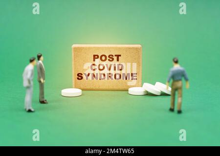 Medizinisches Konzept. Auf der grünen Oberfläche sind Pillen, Miniaturfiguren von Menschen und ein Zeichen mit der Inschrift - Post-Covid-Syndrom Stockfoto