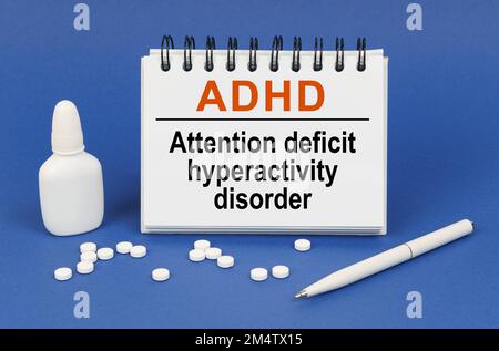 Medizinisches Konzept. Auf blauem Hintergrund ein Stift, Tabletten und ein Notizblock mit der Aufschrift ADHS-Aufmerksamkeitsdefizit-Hyperaktivitätsstörung Stockfoto